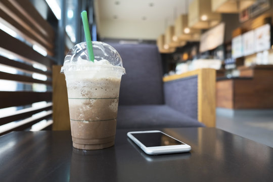 Cold mocha freppe coffee and white cellphone on coffee table in the coffee shop