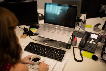 Businesswoman holding coffee cup while working at office desk