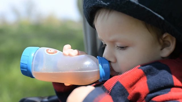 The kid drinks from a bottle