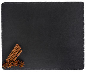 Cinnamon and star anise on a black slate board. Isolated on white background.