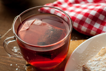 Cup of red fruit tea with teabag in it on a wooden table