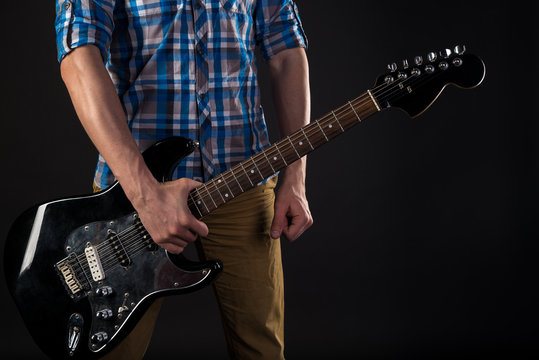 Music and art. The guitarist holds an electric guitar in his right hand, on a black isolated background. Playing guitar. Horizontal frame