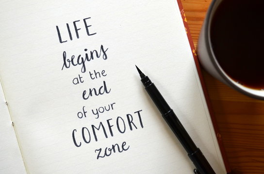 LIFE BEGINS AT THE END OF YOUR COMFORT ZONE written in brush calligraphy on notepad
