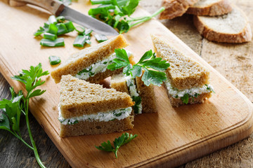 Healthy simple snack made of rye bread, cream cheese, fresh parsley and green onion on a table. Delicious small sandwiches.