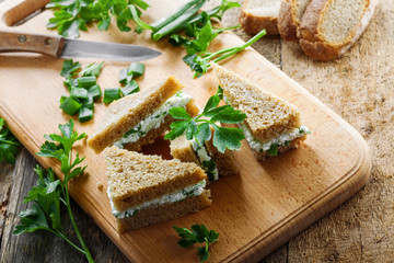 Small sandwiches made of rye bread, cream cheese, fresh parsley and green onion on a table. Simple homemade snack.  Top view.