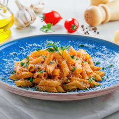 Traditional Italian meal made of penne pasta and arrabiata sauce with parsley on a white table. Delicious healthy Mediterranean food on a blue rustic plate.
