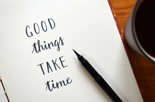 GOOD THINGS TAKE TIME written in notepad on desk with cup of coffee