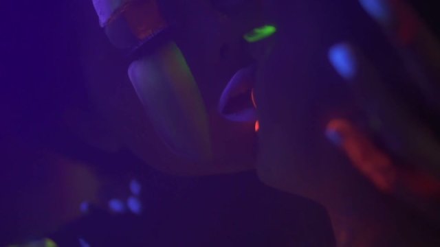 Closeup view of two beautiful girls in fluorescent clothing under UV black light petting each other and kissing