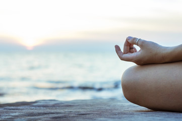 Close up view of hand - meditating in lotus position, sunset and sea on the back ground