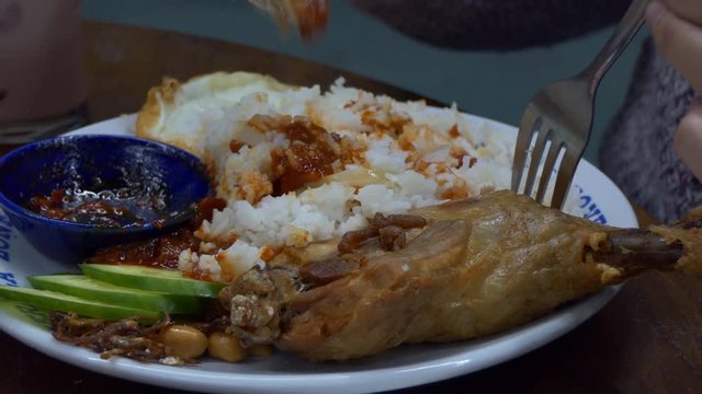 Close up of national Malaysian meal, Nasi lemak, rice cooked in coconut milk with sambal sauce, small fried anchovies, roasted peanuts, fried egg and chicken