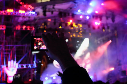 Male hand shoots video by phone during concert with laser show at night