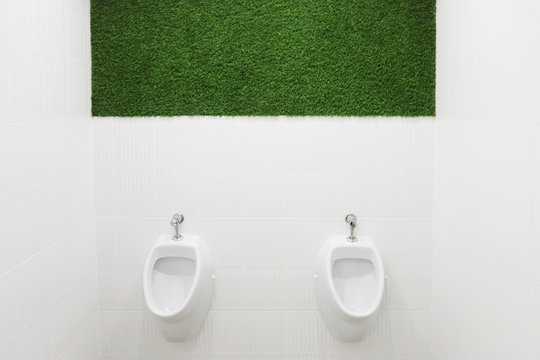 Two white urinals in empty male toilet with green lawn on wall
