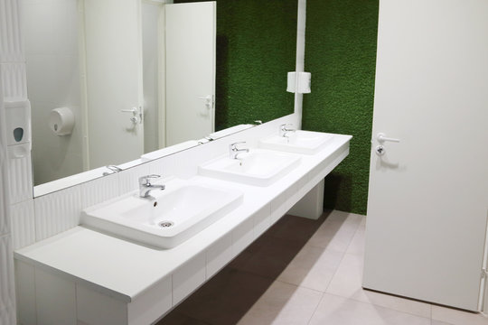 Three white sinks in toilet with big mirror and green lawn wall