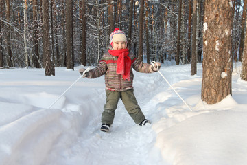 Fototapeta na wymiar Happy handsome little boy with red scarf skis in forest at sunny day