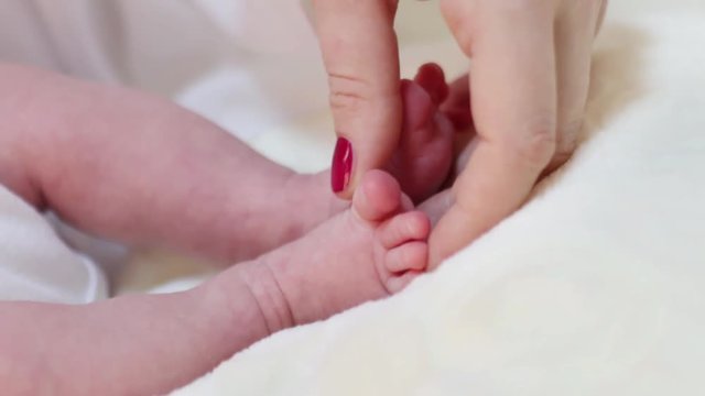Woman hand touches funny little feet of baby on bed in room