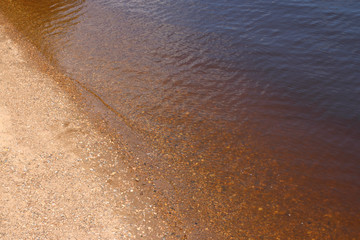 Transparent water of river with highlights and yellow sand at summer day