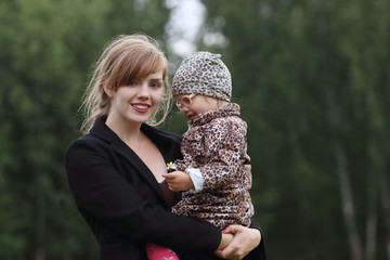 Young pretty woman holds little daughter outdoor at summer day