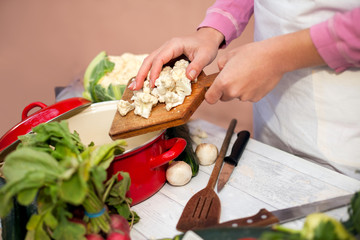 Woman putting sliced cauliflower in kitchen dish