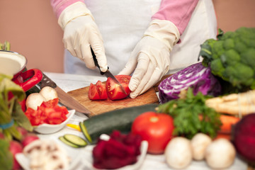 Housewife with gloves slicing tomato
