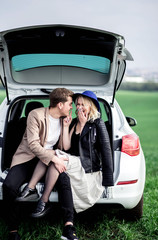 The boy and the girl sit on a car trunk and laughing