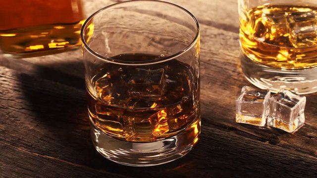 pouring whiskey into a glass with ice cubes on old wooden table