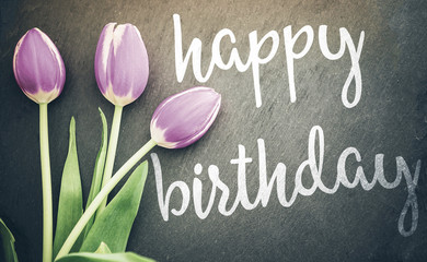 birthday greeting card top view of pastel purple tulips on dark gray slate blackboard background