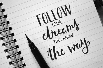 FOLLOW YOUR DREAMS THEY KNOW THE WAY inspirational quote written in notebook