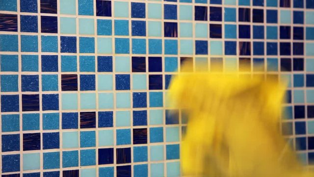 Person doing chores in bathroom at home cleaning tiled wall with sprayer and microfiber towel