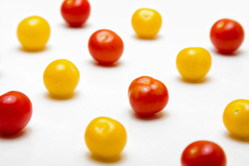 Red and yellow cherry tomatoes on a white background, in perspective view. Shallow depth of field.