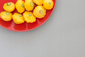 Pattypan squash bright yellow color on a red plate. Image of a vegetable with a place for an inscription.
