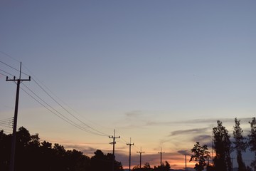 Fototapeta na wymiar Electricity poles at the roadside with beautiful blue sky before sunset,Photos back-light at the horizon began to turn orange