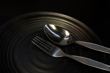 Low key, Fork and spoon on black dish in low light restaurant.