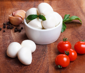 Cherry mozzarella in bowl, cherry tomatoes,fresh basil, garlic and pepper on wooden board.