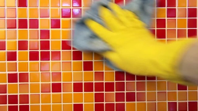 Person doing chores in bathroom at home cleaning tiled wall with sprayer and microfiber towel