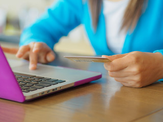 Fototapeta premium Pretty Young womans hands holding a credit card and using laptop computer for online shopping. Online payment. Female working on laptop in a cafe.
