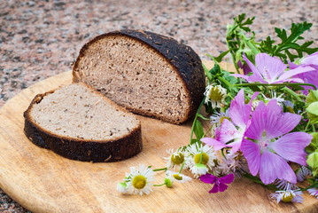 Loaf of rye bread with caraway seeds and wild flowers on cutting board