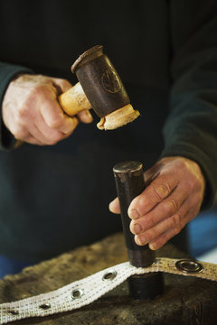 Close up of a man in a sailmaker's workshop, hammering eyelets into a strip of sailcloth.