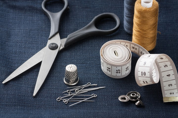 Scissors, Thimble, Pins, Centimeter Tape, Thread, Button On Black Jeans Fabric Close Up And Top View.
