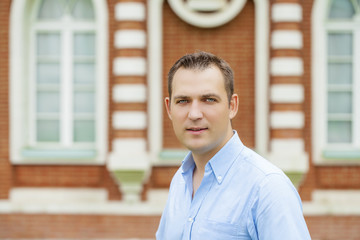 Young handsome man in a blue shirt on the background of summer park
