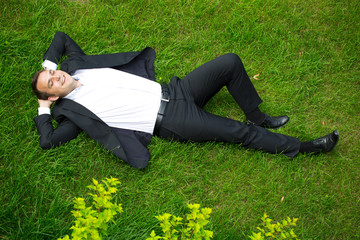 Young businessman in a suit lying on the grass, view from above