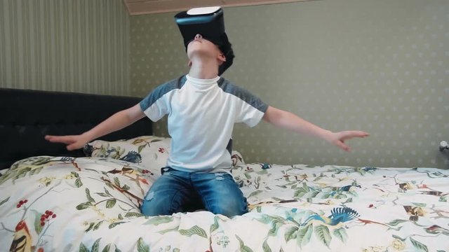 Little boy using virtual reality headset in the flight simulator sitting on the bed