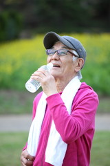 屋外での運動の合間にペットボトルの水を飲むシニアの男性