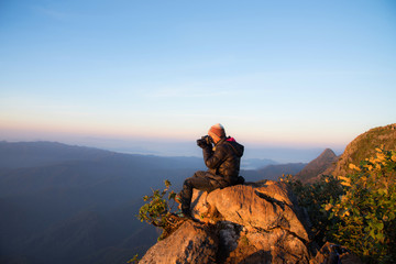 A man sitting on stone and shooting sunrise view of beautiful mountains.