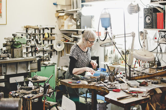 Senior female craftsperson working at workbench in jewelry workshop