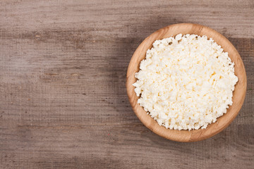 Cottage cheese in a wooden bowl on old wooden background with copy space for your text. Top view