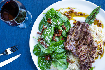 Gourmet restaurant lunch with tenderloin steak served on fresh spinach leaves with brown rice and a glass of red wine.  Top view, deep blue background.