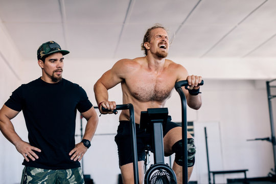 Bodybuilder spinning stationary bike in gym with personal trainer