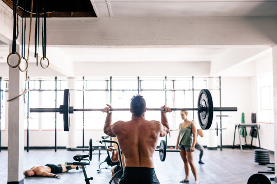 Rear view of man lifting barbell at gym