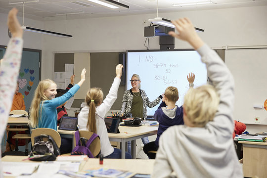 Teacher looking at students with hands raised in classroom
