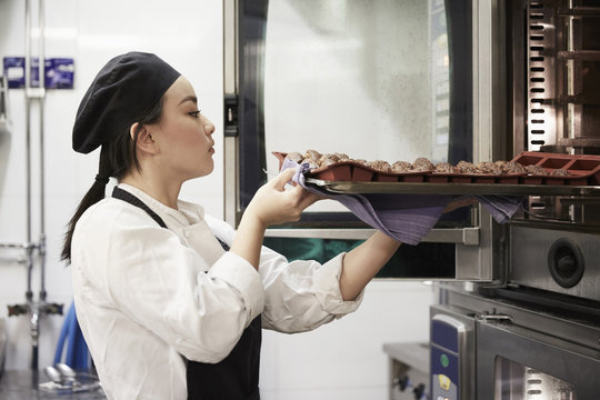 Side view of female chef taking out tray of cookies from oven at commercial kitchen